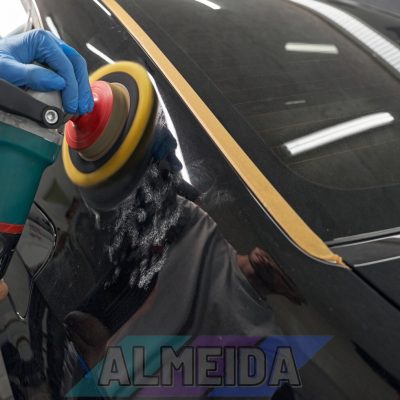 Close up of hands worker using polisher to polish black car body in workshop