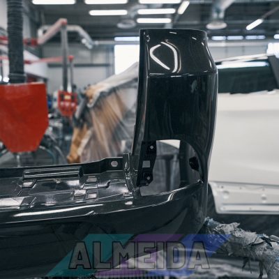 Detached bumper lying in car workshop with with repair equipment standing in the background